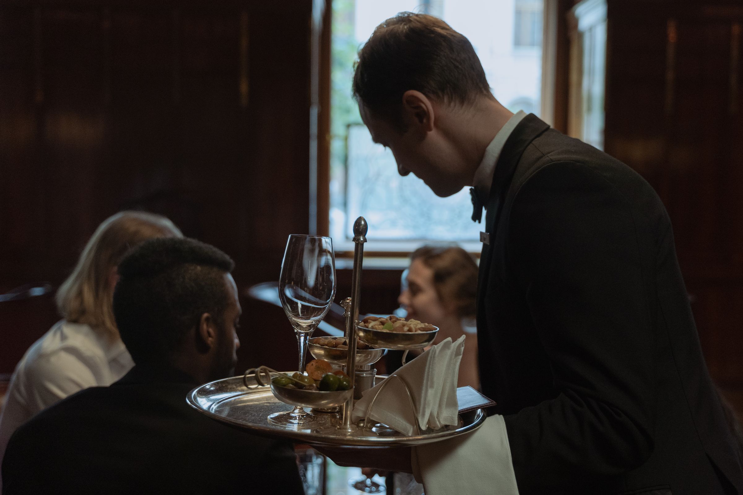 A waiter carrying a tray of drinks and canapés to guests in a restaurant